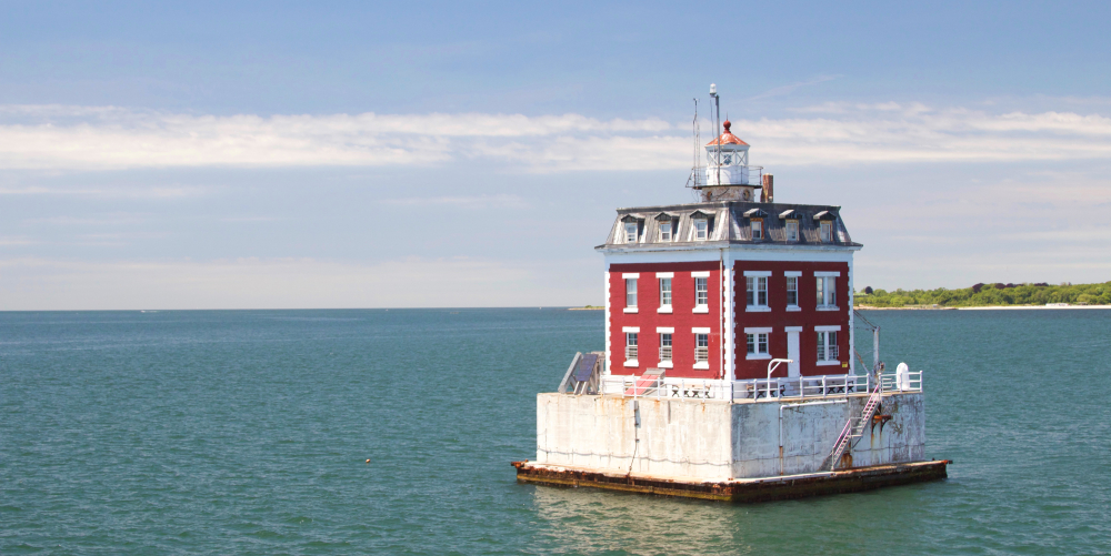 Red and white lighthouse on concrete base in calm sea under blue sky