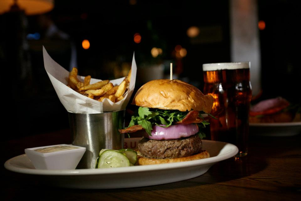 Burger with fries, pickles, dipping sauce, and two glasses of beer