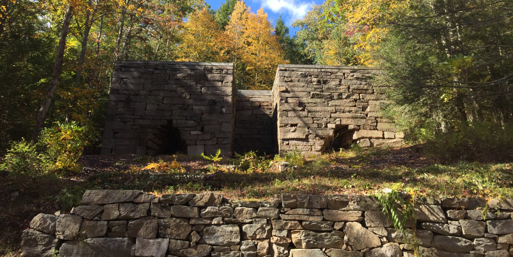 Historic stone furnace ruins surrounded by autumn trees under blue sky