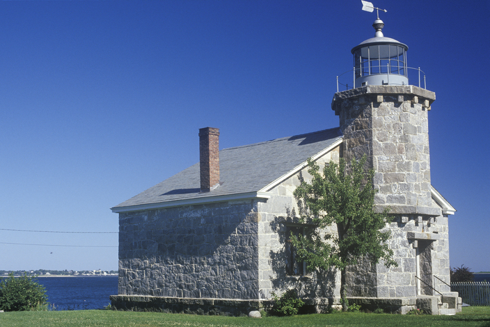 Historic stone lighthouse museum by water under clear blue sky