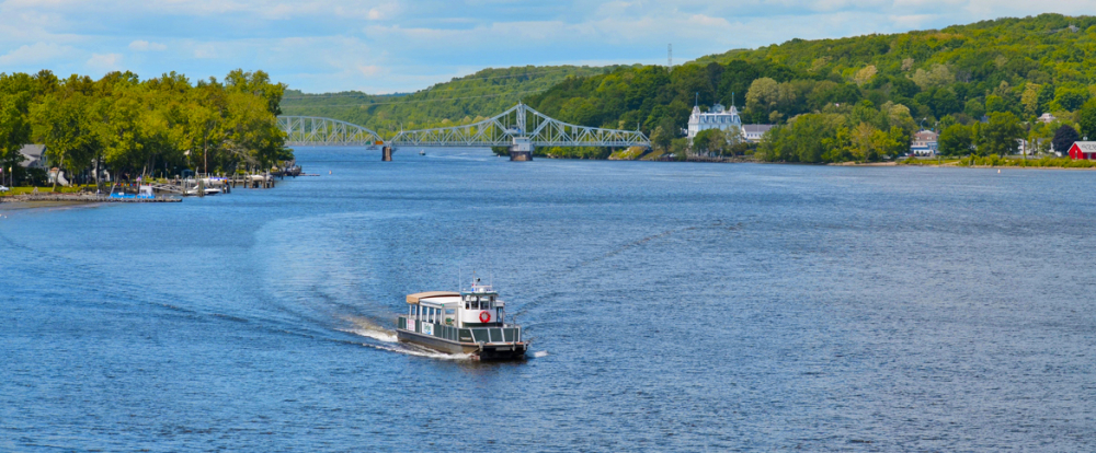 Boat cruising on river with bridge and green trees in Haddam