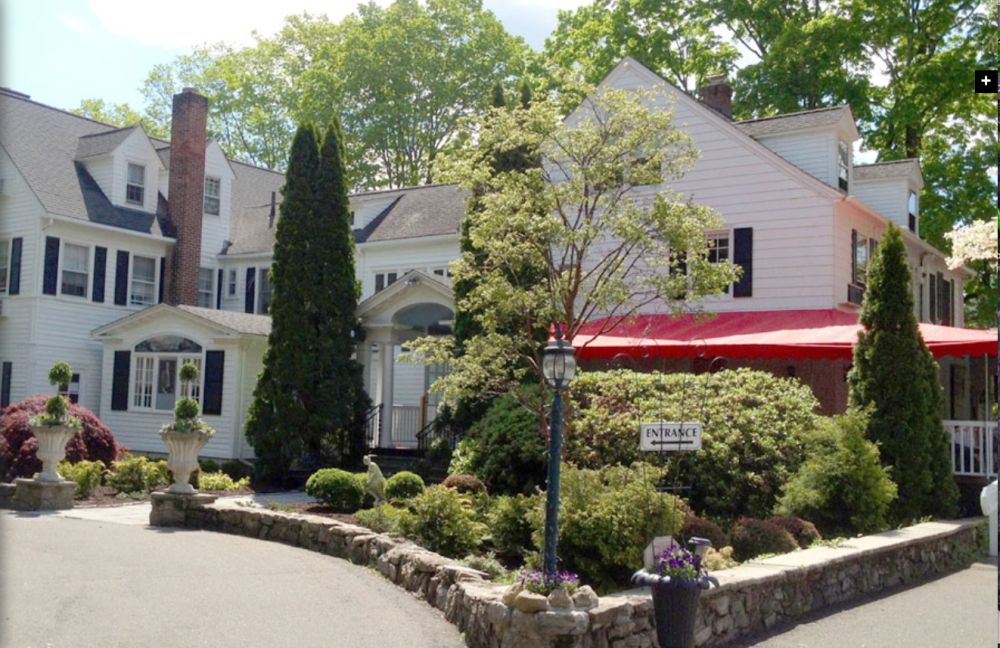 White colonial inn with red awning and landscaped garden entrance