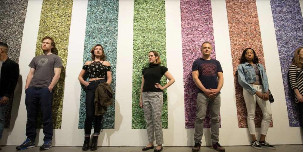 Seven people standing against a wall with vertical colorful photo strips