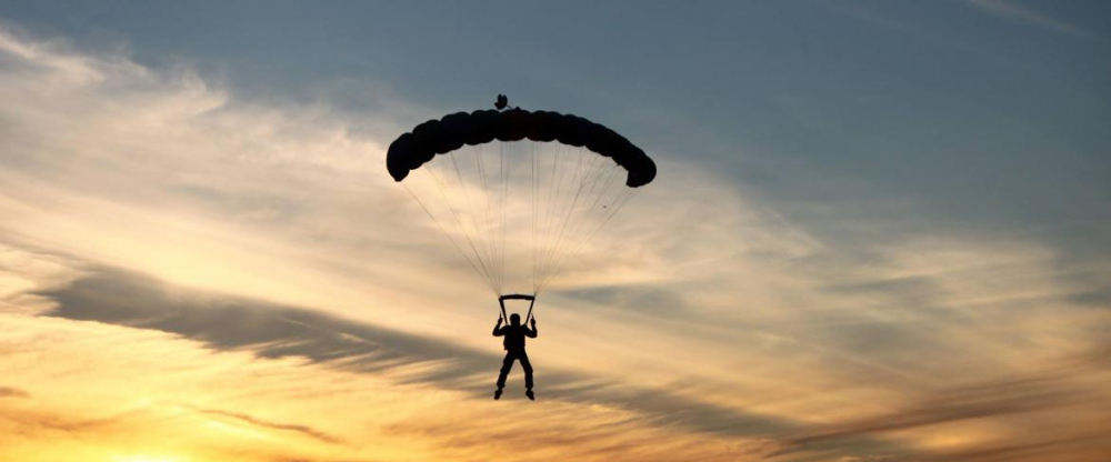 Silhouette of a skydiver descending with parachute at sunset