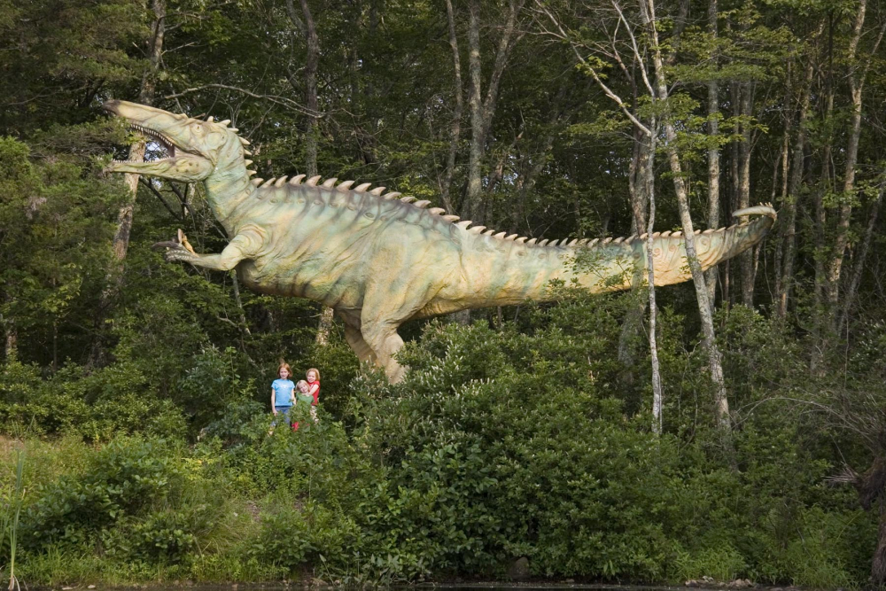 Large Suchomimus dinosaur model with three children in wooded area