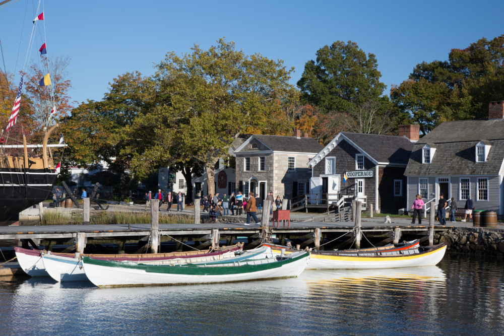 Historic seafaring village with boats docked by wooden pier and people nearby