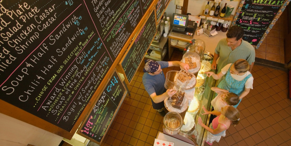 Cafe staff serving three customers at a baked goods counter with menu boards
