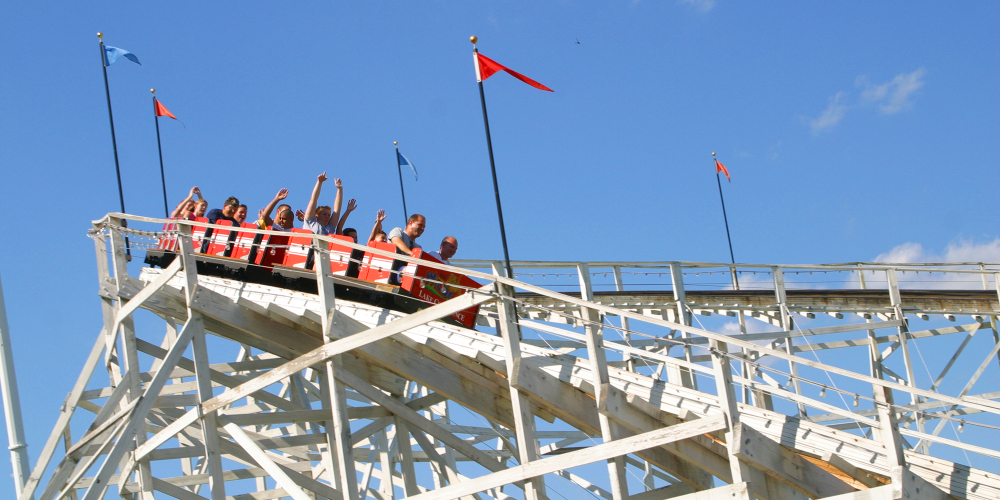 People riding a wooden roller coaster under blue sky