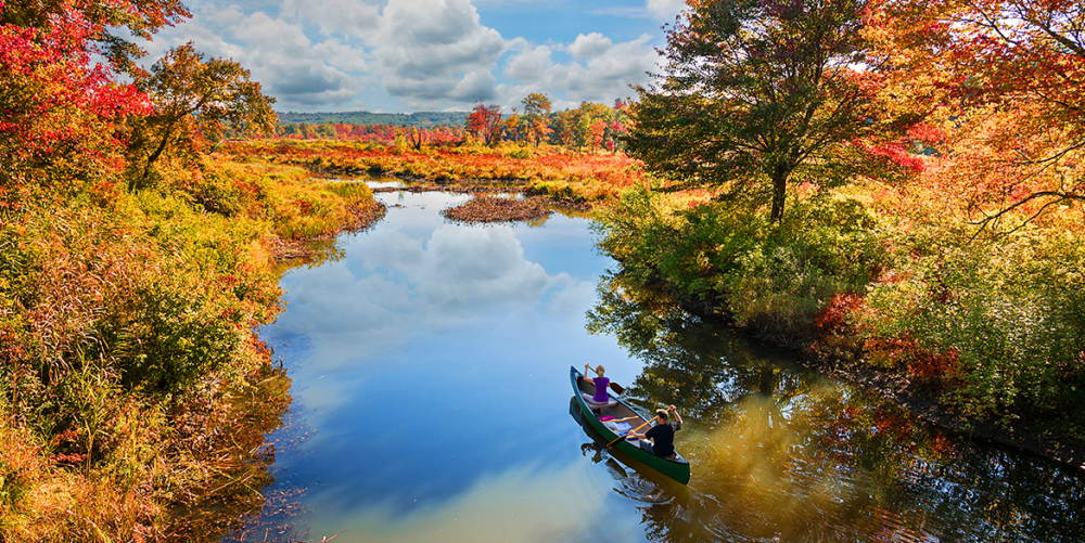 Two people paddling canoe on Bantam River in autumn foliage