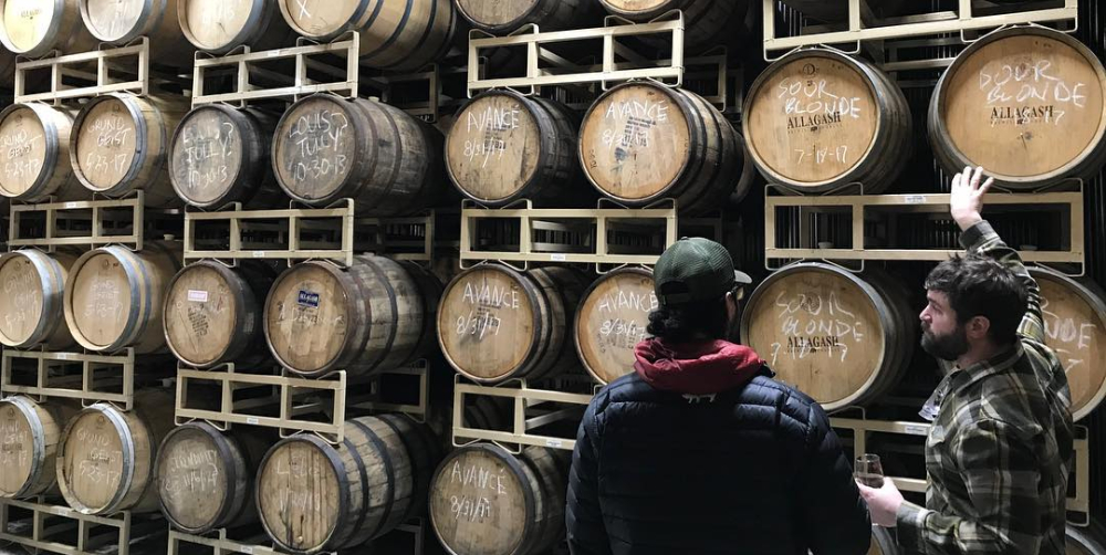 Two men examining wooden barrels stacked in storage racks