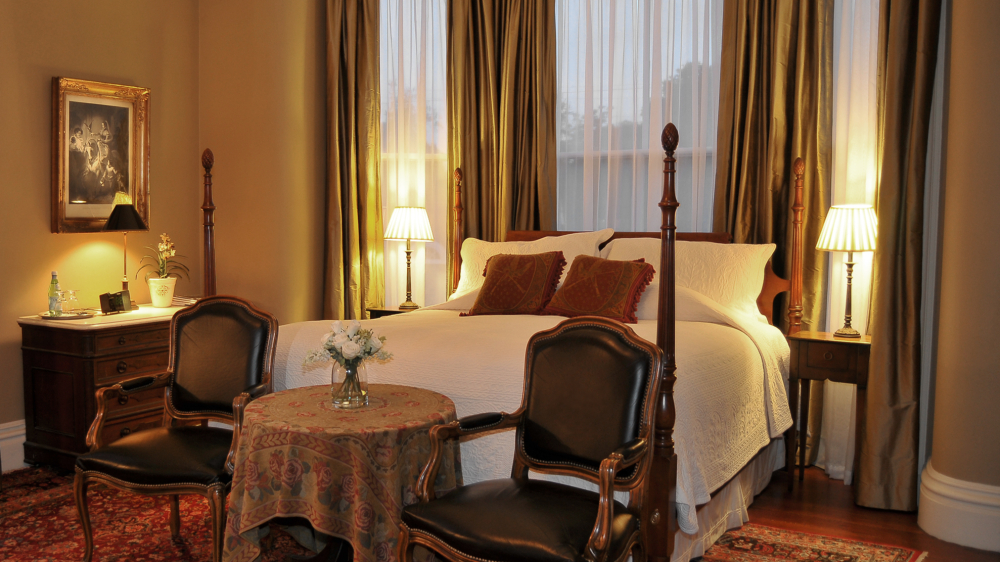 Elegant bedroom with four-poster bed, vintage chairs, and warm lighting