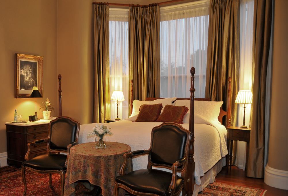 Elegant bedroom with four-poster bed, vintage chairs, and warm lighting