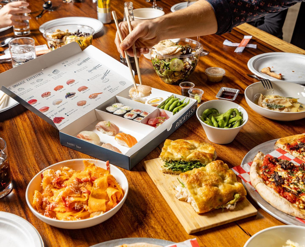 Variety of sushi, pasta, sandwich, pizza, and salad on wooden table