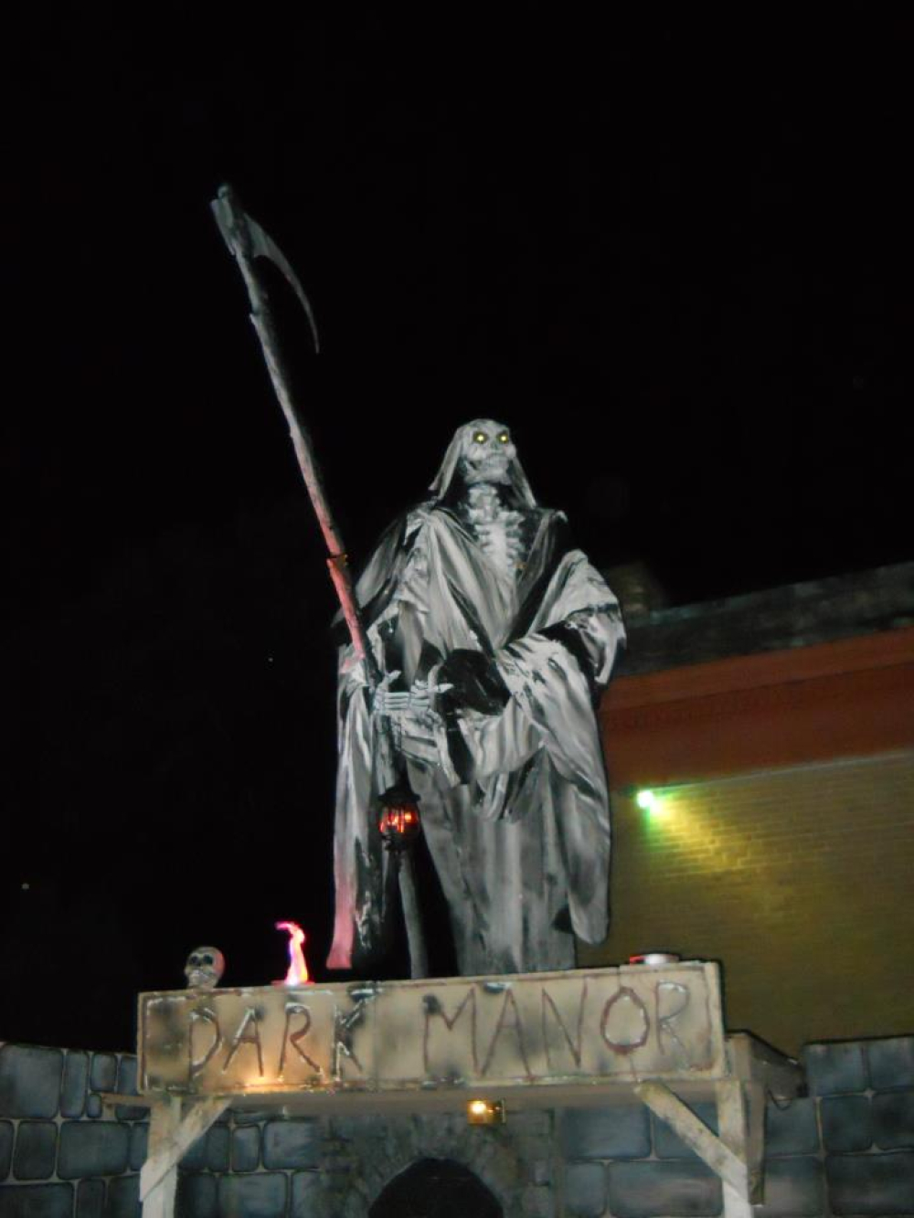 Grim Reaper statue holding a scythe above Dark Manor sign at night