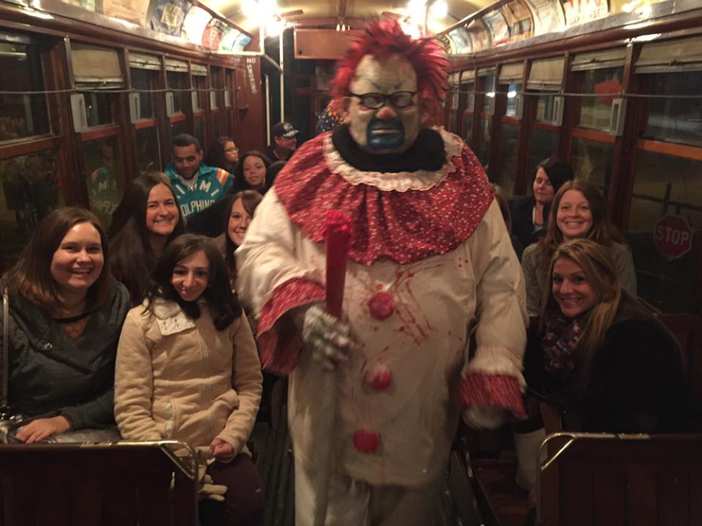 Person in scary clown costume holding a red bat on a vintage train with