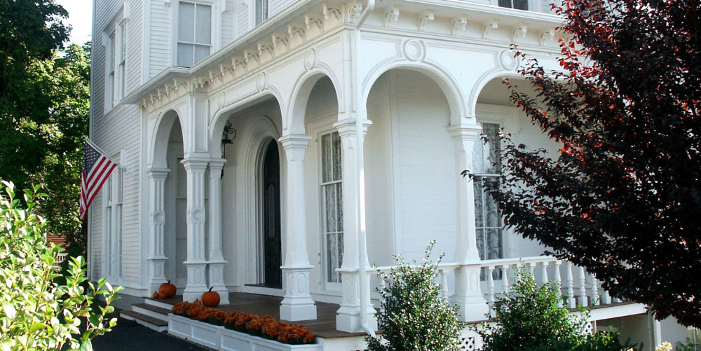 White Victorian house porch with pumpkins and American flag in fall