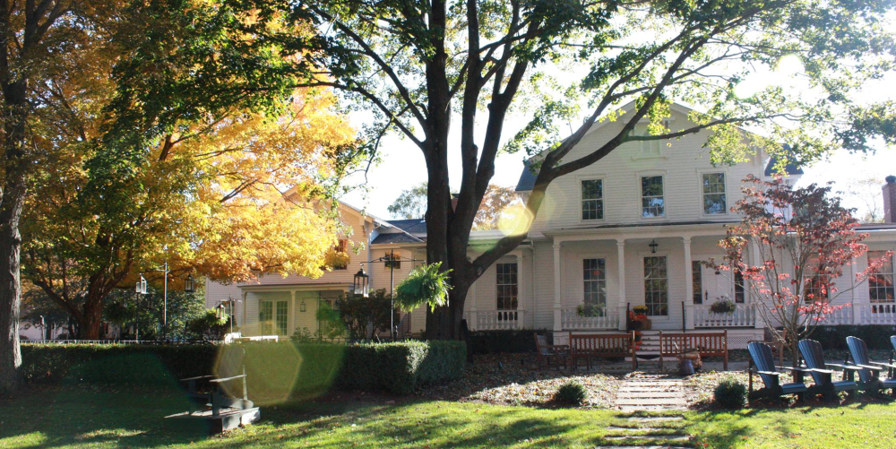 White house with porch amid autumn trees and lawn chairs on green grass