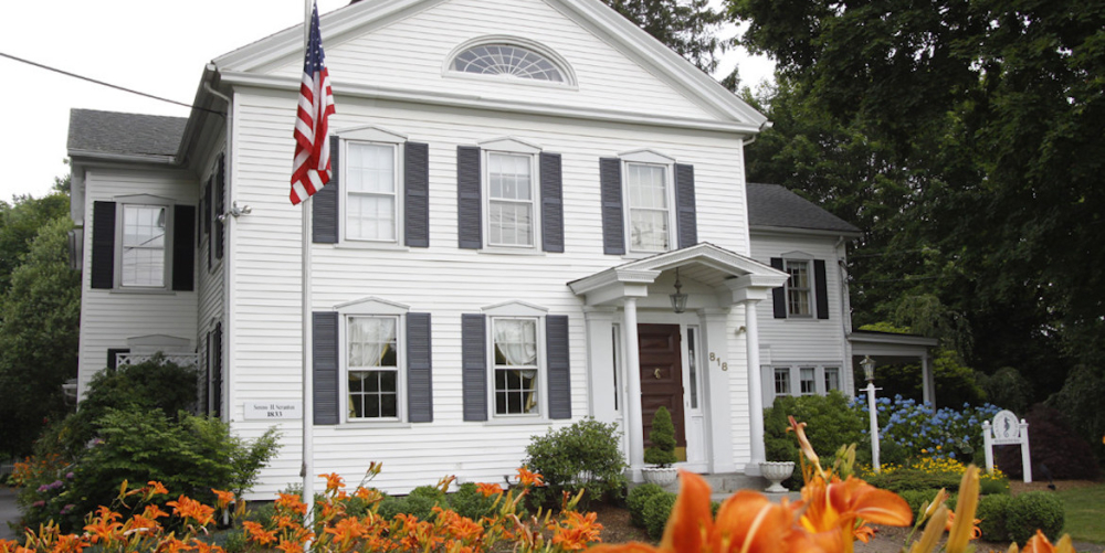 White colonial house with black shutters surrounded by orange lilies
