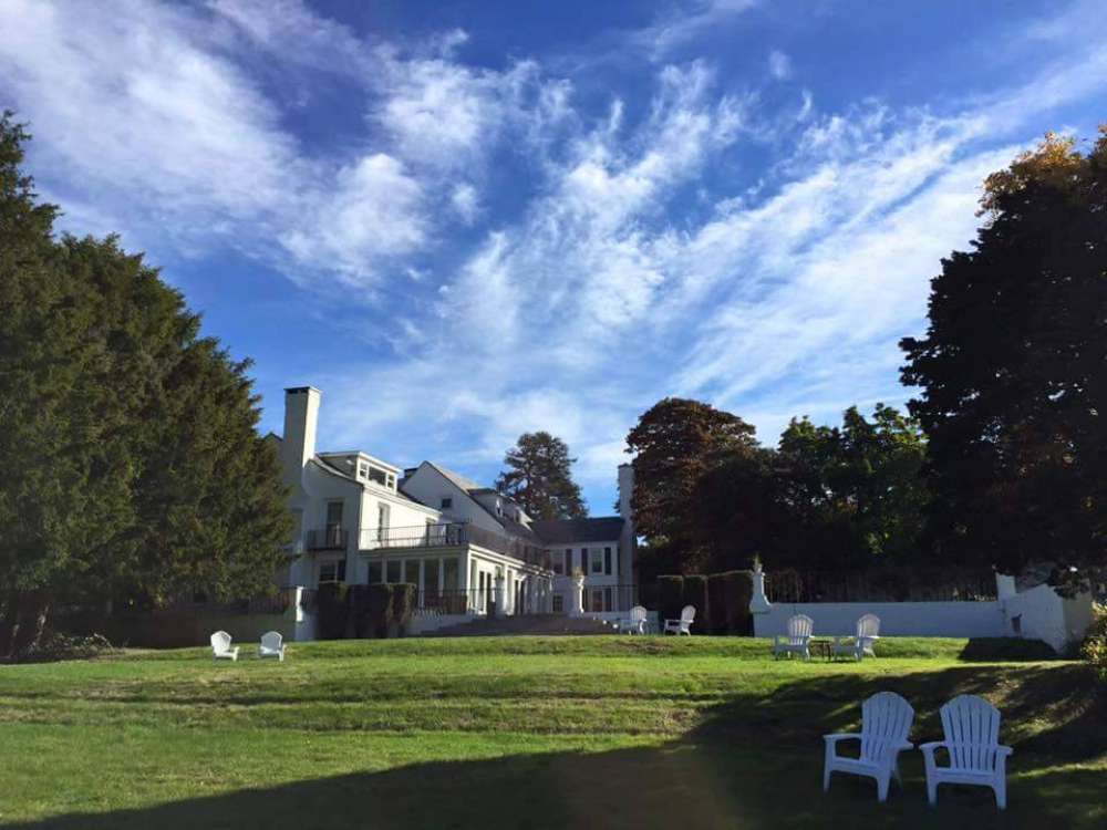 Large white house with lawn and Adirondack chairs under a blue sky