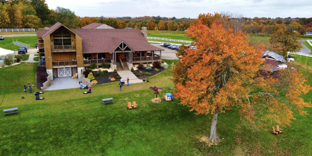 Large wooden lodge with people, fall foliage tree, and green lawn