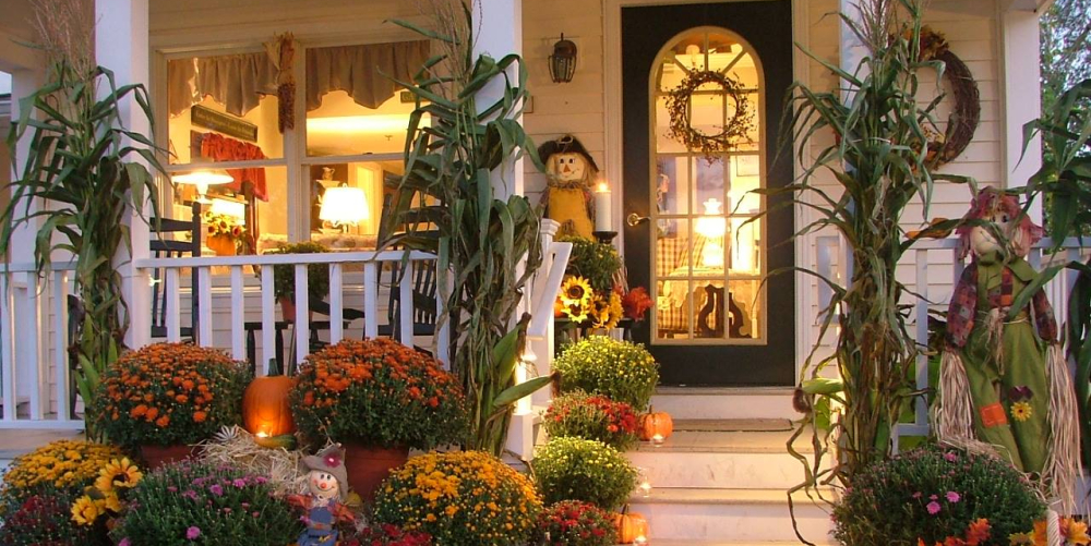 Fall-decorated porch with pumpkins, mums, cornstalks, and scarecrows