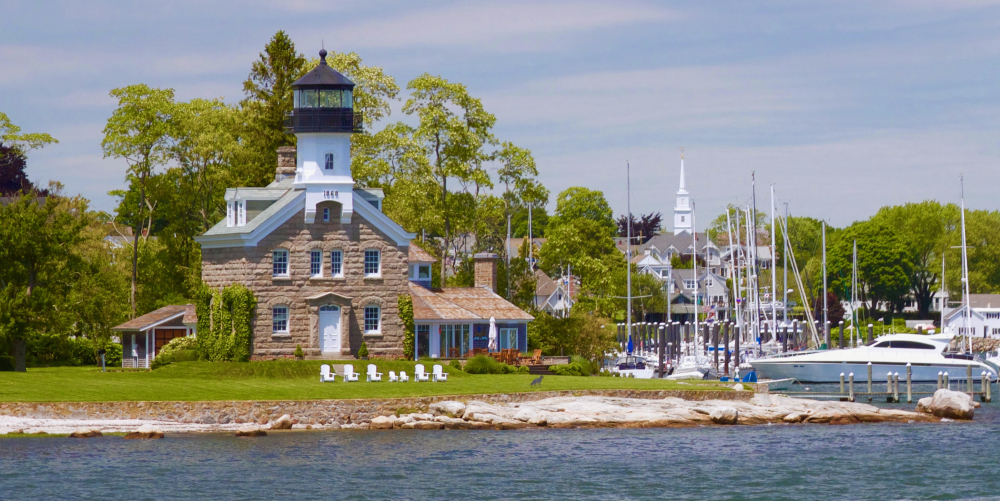 Stone lighthouse near marina with boats and trees on sunny day