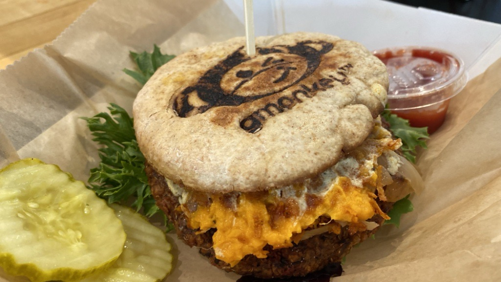 Una hamburguesa con queso vegana de G-Monkey Fast Food, con un logotipo estampado en el pan.