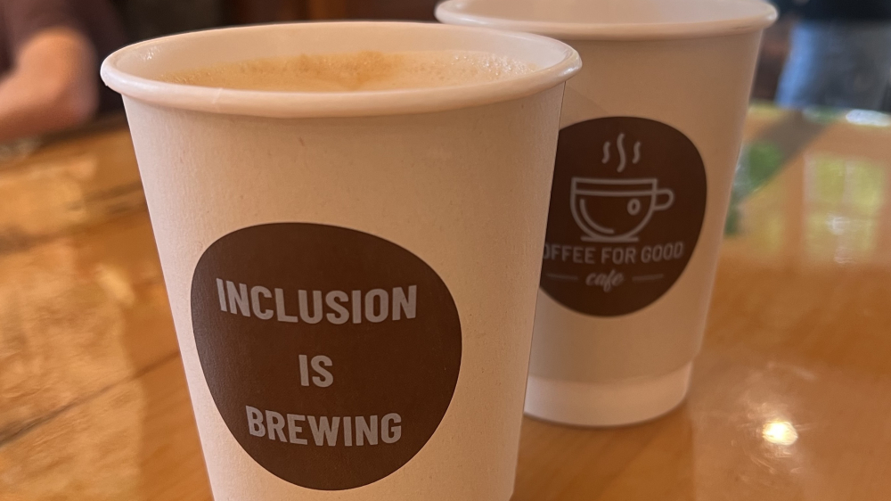 Una taza de café de Coffee For Good en Greenwich, con el texto "La inclusión se está gestando"