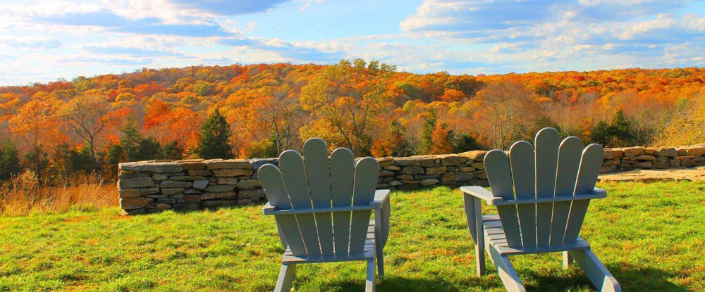 Two Adirondack chairs facing colorful autumn forest on a ridge