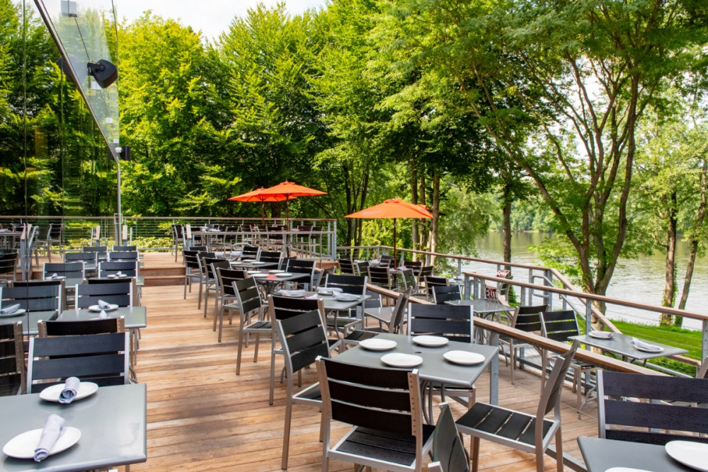 Outdoor restaurant seating on wooden deck overlooking river and trees