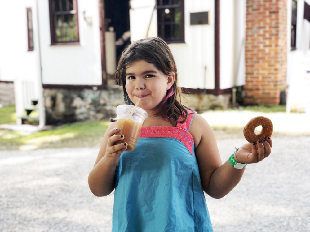 Child sipping cider and holding a donut outside a building