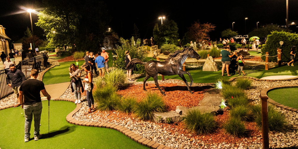 Nighttime mini golf course with people and a horse statue