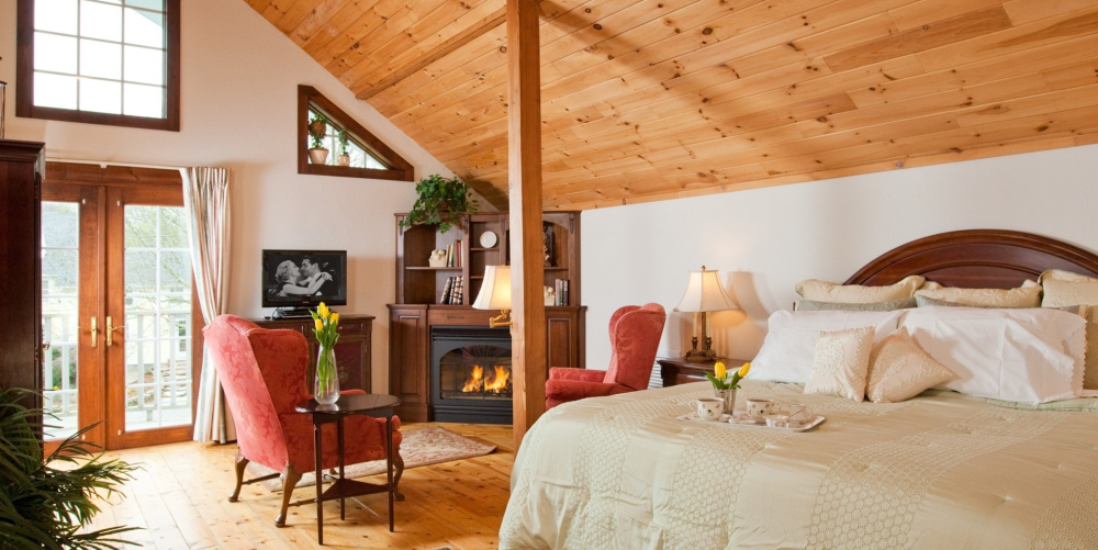 Cozy bedroom with wooden ceiling, fireplace, and sitting area with red chairs