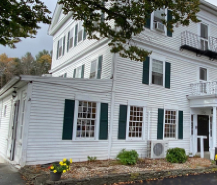 Large white colonial building with green shutters and small garden
