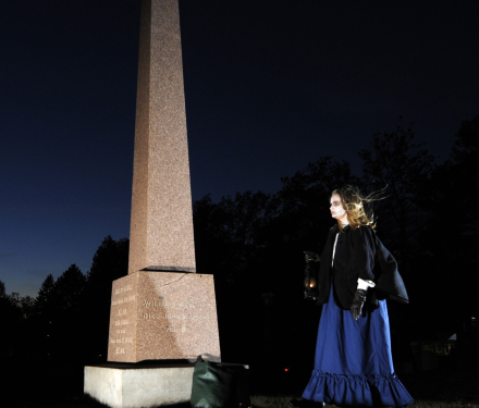 Person holding lantern near tall grave monument at night