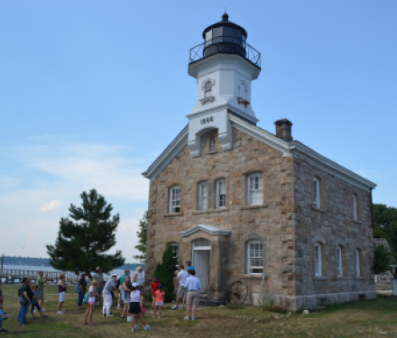 Stone lighthouse with people gathered outside near waterfront