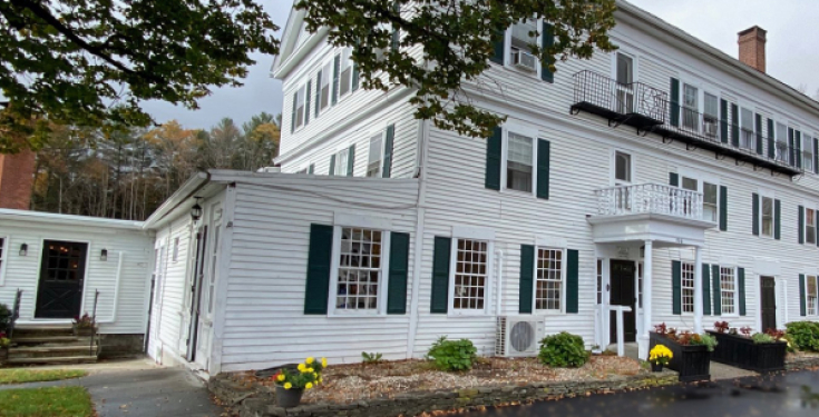 Large white colonial building with green shutters and small garden