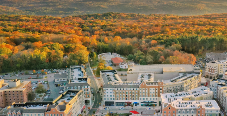 An aerial view of a downtown neighborhood with rolling hills emblazoned in fall colors in the distance