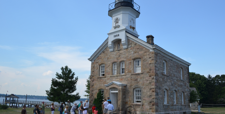 Stone lighthouse with people gathered outside near waterfront