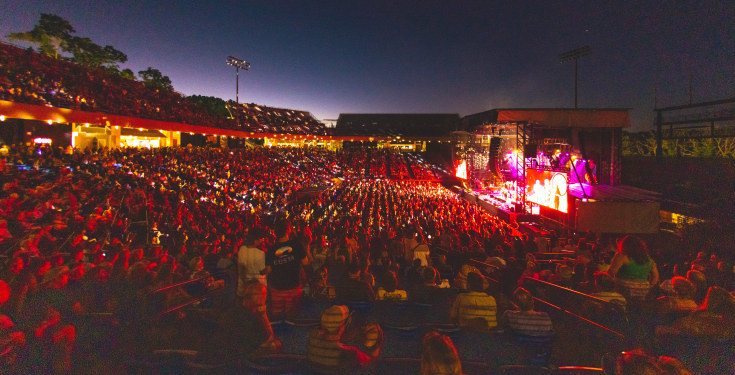 Large crowd watching a nighttime concert at an outdoor stadium